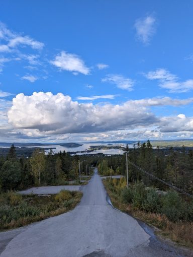 Aussicht von einem Turm in die Ferne. Viele Seen im Hintergrund zu sehen, vorne eine lange Straße, die Richtung Seen läuft